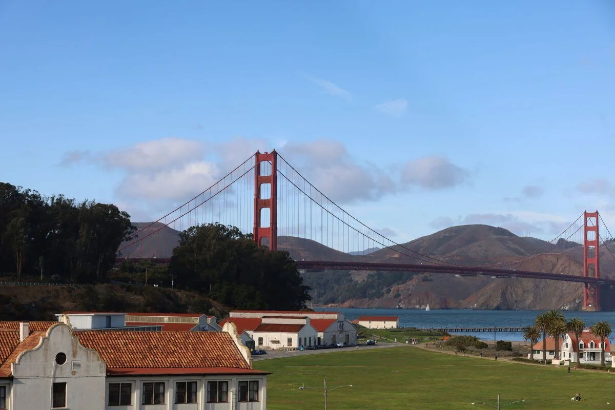 Historic military buildings and open lawn at Crissy Field in the Presidio, with the Golden Gate Bridge and Marin Headlands in the background