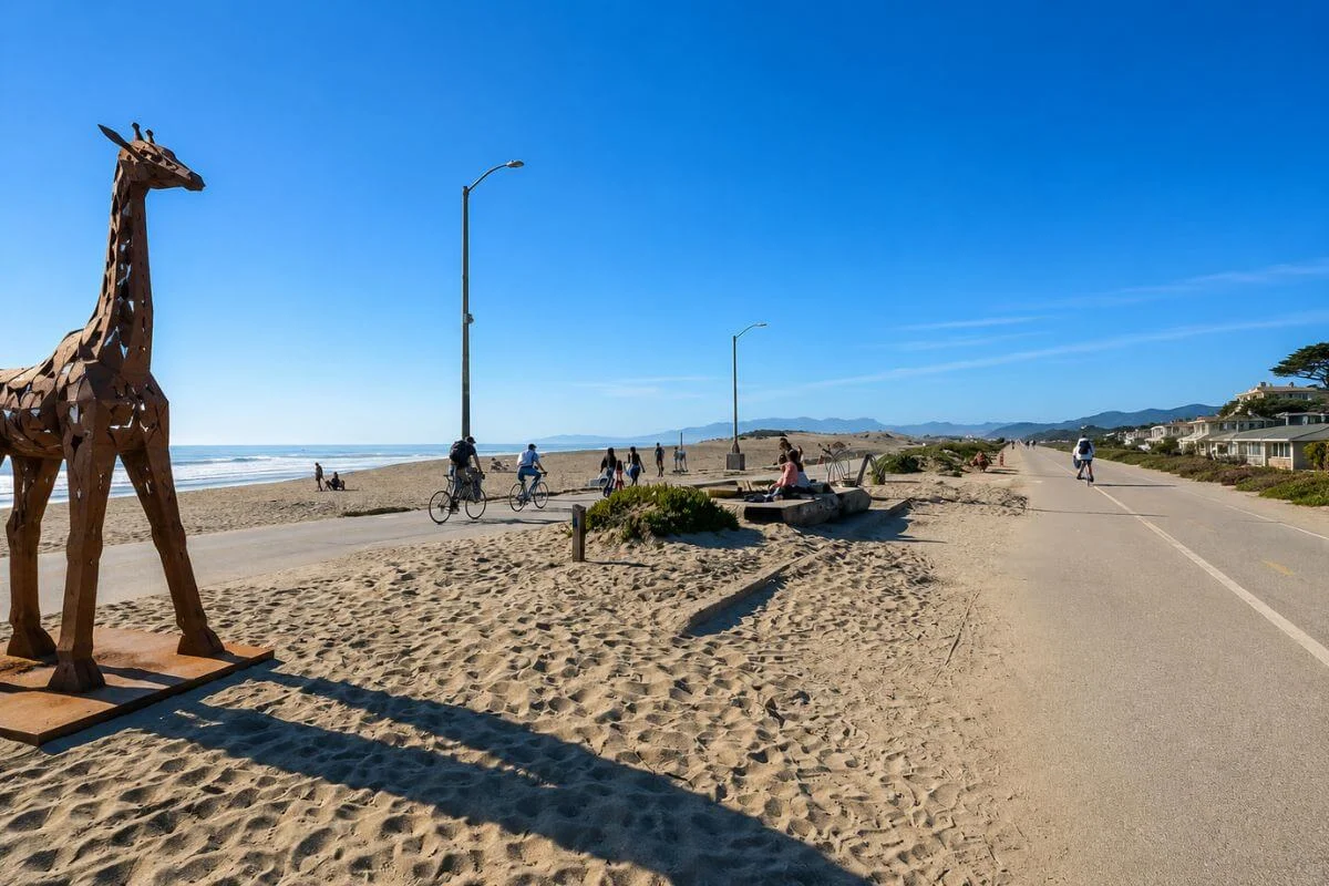 Wooden giraffe sculpture beside paved beach path with cyclists and ocean view