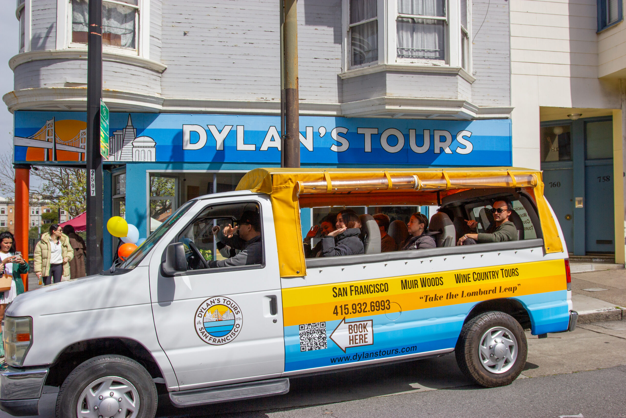Branded Dylan's Tours van with open roof carrying tourists outside San Francisco storefront