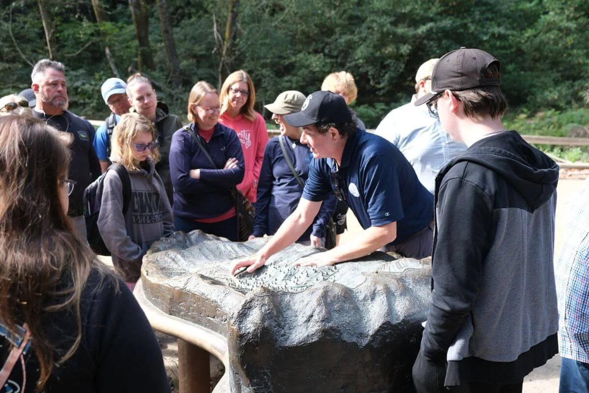 Tour guide pointing at a bronze relief map while a group of visitors listens at Muir Woods
