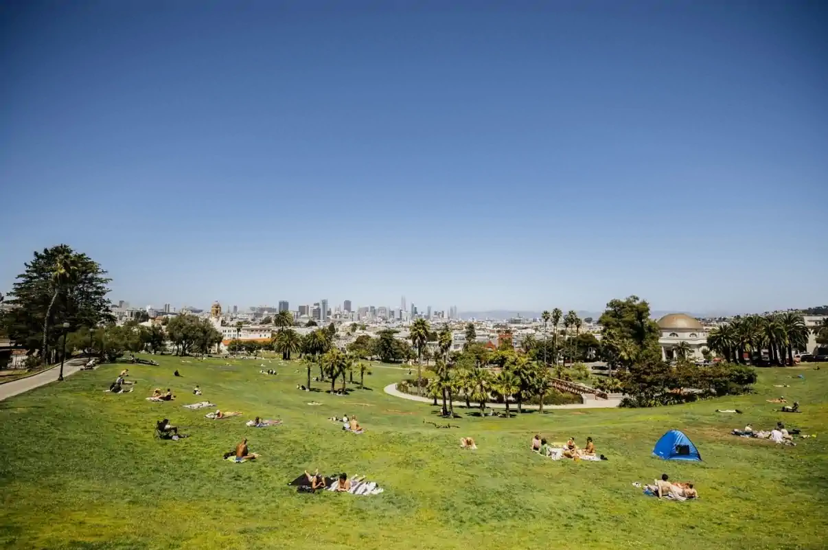 People relaxing on the lawn at Dolores Park with San Francisco skyline