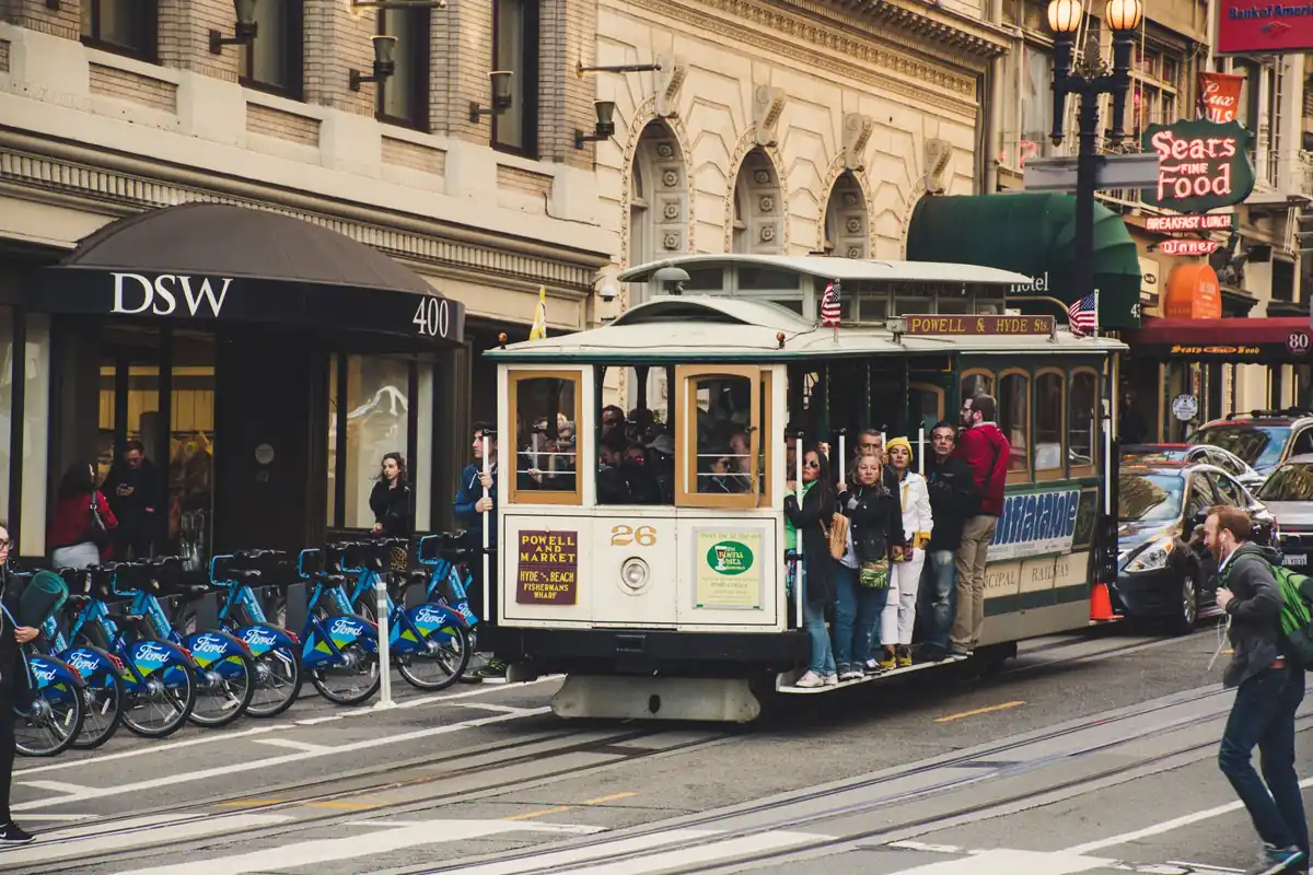 Crowded Powell-Hyde cable car with riders hanging off the side, passing Sears Fine Food on Powell Street in San Francisco